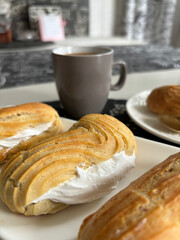 Homemade eclairs on a plate. A cup of coffee nearby. Close-up.