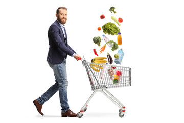 Bearded guy walking and pushing a shopping cart with groceries falling