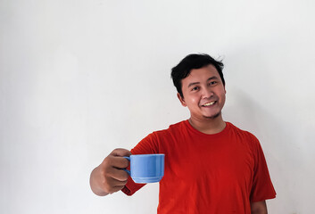 man holding a cup of coffee, Asian man sipping coffee with blue cup, smiling Asian man sipping coffee, Indonesian man drilling using cup with amazed expression or Amazed expression.