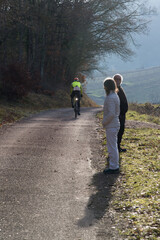 Obraz premium un couple sénior regarde un cycliste sur son vélo en hiver dans le vignoble. Balade en hiver dans les vignes. Randonnée sur une route de campagne.