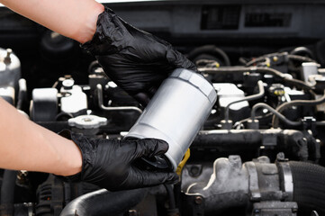 Auto mechanic repairman in working gloves holds fuel filter for diesel cars against background of...