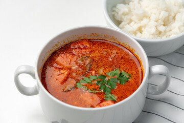 Bowl of curry with pieces of meat and a side of steamed rice arranged neatly for a meal
