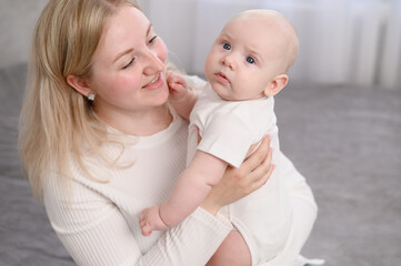 Loving mom holds newborn in her arms, hugging her, caring for baby. Mother looks at infant with love. Concept of motherhood, family, childhood, maternity leave, caring for baby.