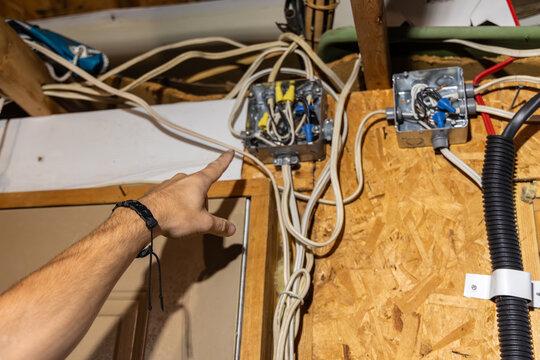 Electrician is pointing at an electrical box with exposed wires during an inspection in an attic. Selective focus