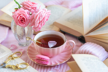 A cup of aromatic tea, a book and a rose on the table.