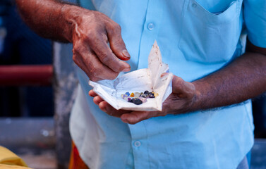 An individual at the Nivithigala gem market in Sri Lanka presents a collection of rough gemstones wrapped in paper for evaluation. He is negotiating with another person to secure a better price.