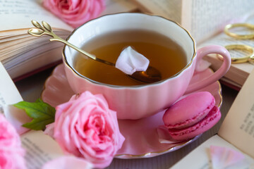 A cup of aromatic tea, a book and a rose on the table.