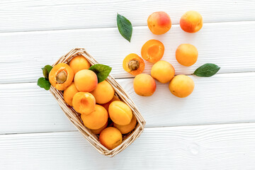 Fresh raw apricots in basket on white wooden background top view pattern with leaves