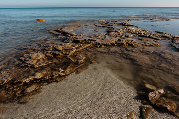 Calm Lake Michigan water washes over the rocky bordered beach in early Febuary, during an unseasonably warm winter at Harrington Beach State Park, Belgium, Wisconsin