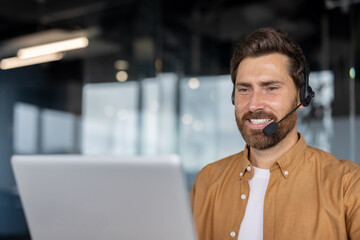 Smiling businessman in office wearing headset working on computer. Professional engaged in remote...