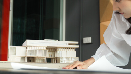 Closeup of asian young beautiful architect engineer looking at project plan with model placed on table. Professional project manager analysis house structure. Business design concept. Manipulator.