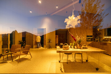 View through the window of a cozy, warmly lit cabin interior. Reflections of the outside trees merge with the inviting decor, creating a unique interplay of inside and out