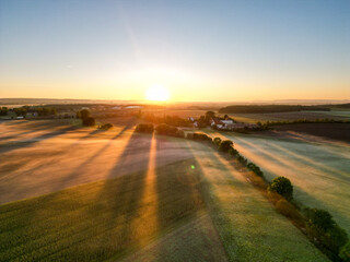 Sonnenaufgang über Schweinfurt mit Nebelschleiern, Nebel über den Feldern, mit einem Bach und Bäumen und die aufgehende Sonne am Horizont, Drohnenfoto, Luftaufnahme, Schweinfurt, Bayern, Deutschland	
