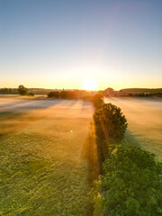 Sonnenaufgang über Schweinfurt mit Nebelschleiern, Nebel über den Feldern, mit einem Bach und Bäumen und die aufgehende Sonne am Horizont, Drohnenfoto, Luftaufnahme, Schweinfurt, Bayern, Deutschland	

