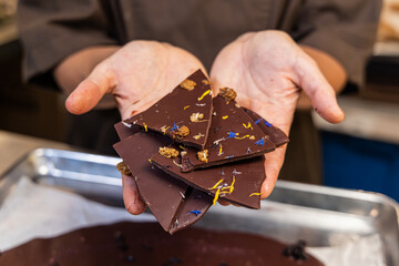 Chocolatier presenting a selection of artisanal chocolate pieces adorned with edible flowers and nuts. Selective focus