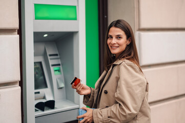 Smiling woman withdrawing money from atm on street