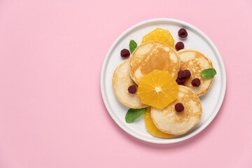 Pancakes with orange and raspberries in plate top view on pink background with copy space. Morning traditional breakfast