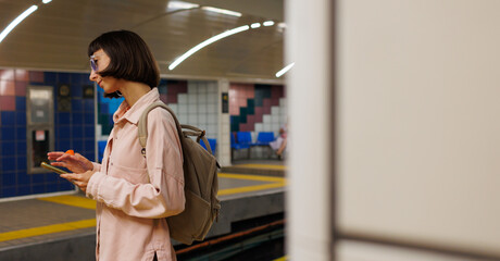 Young girl with a backpack uses a smartphone in the subway. girl waiting for a train.