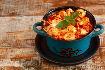 Tortellini bake with mozzarella and parmesan cheese, tomato sauce in baking dish on dark wooden table