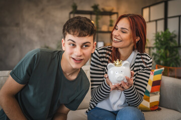 happy young couple sit on sofa and save money coins in the piggy bank