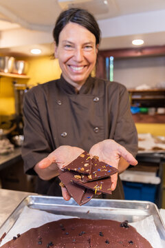 Chocolatier woman smiling and holding pieces of dark chocolate with nuts and flowers in her hands. Selective focus