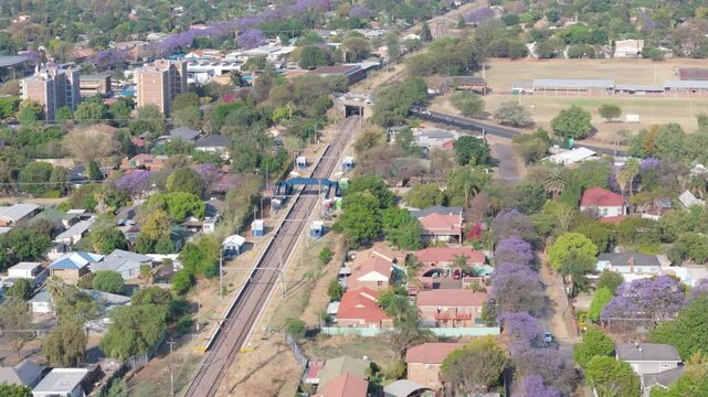 Aerial: passenger railway line through Pretoria residential suburb with jacaranda trees, Sideways jib and orbit