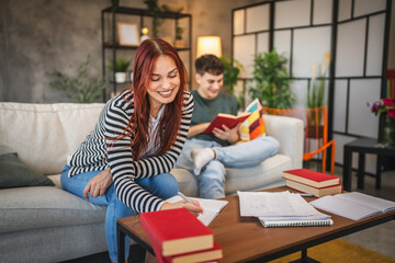 Adult woman write notes for exam, while adult man read a book