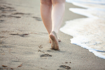 Closeup image of beautiful young barefoot woman walking in the calm warm sea waves against amazing sunset