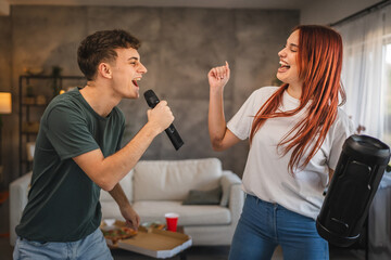 Young adult cheerful couple sing and dance at home on karaoke party