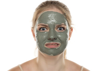 Disappointed funny young woman posing with a facial green mud mask on her face. Skin care and treatment, spa, natural beauty and cosmetology concept