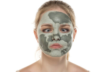 Funny young woman posing with a semmy-dried facial green mud mask on her face. Skin care and treatment, spa, natural beauty and cosmetology concept