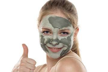 Young smiling woman posing with a semmy-dried facial green mud mask on her face. Skin care and treatment, spa, natural beauty and cosmetology concept