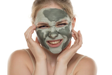 Young funny woman posing with a semmy-dried facial green mud mask on her face. Skin care and treatment, spa, natural beauty and cosmetology concept