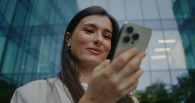 Positive Caucasian woman talking out her mobile device from pocket and pressing on touch screen. Placing smartphone back into pocket while smiling. Receiving positive notification.