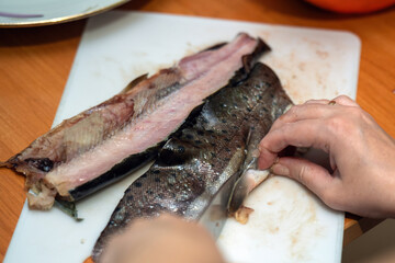 woman's hands meticulously clean a fish, deftly cutting off its fins. This intimate act showcases...