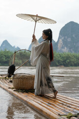 Hanfu girl with deng looking at mountainous landscape from raft on Li river, China. Vertical