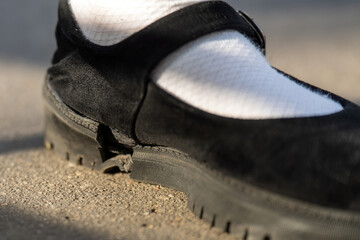 close-up reveals a foot clad in a white sock and black shoes with a cracked sole, symbolizing wear...
