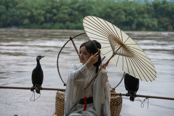 Hanfu girl fixing her hair and holding parasol while standing on bamboo raft by Li river