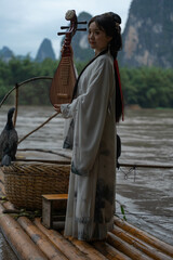 Young woman in Hanfu playing pipa on a Bamboo Raft. Xingping, China. Vertical shooting