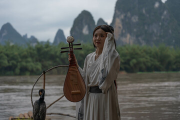 Hanfu girl poses with Pipa on bamboo raft with a mountainous background. Xingping, China