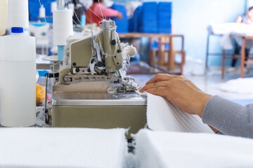 Manos expertas cosiendo tela blanca en una máquina overlock, Detalle de una operación de costura...