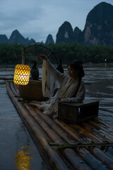 Hanfu Girl holding a lantern on a bamboo raft, Xingping, China. Vertical