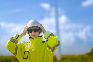 An engineer in high visibility work gear and a hard hat points toward a wind turbine in the...
