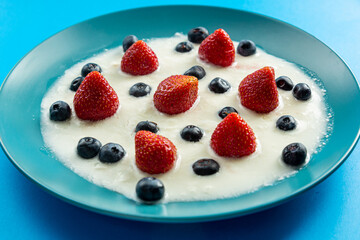 Fresh juicy berries strawberries and blueberries in a blue plate with whipped cream on a blue background