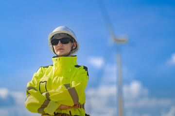 An engineer in high visibility work gear and a hard hat points toward a wind turbine in the...
