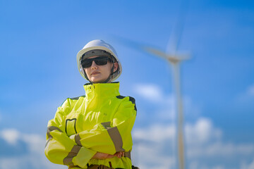An engineer in high visibility work gear and a hard hat points toward a wind turbine in the...