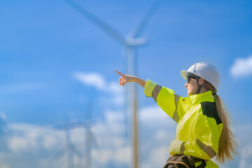 An engineer in high visibility work gear and points toward a wind turbine in the background. The scene highlights renewable energy and the professional's involvement in wind farm operations.