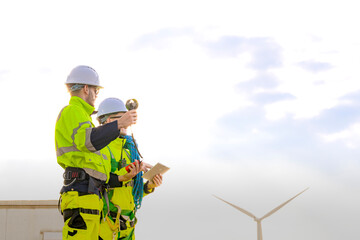 Two engineers wearing high visibility safety jackets and helmets measure wind speed with an...