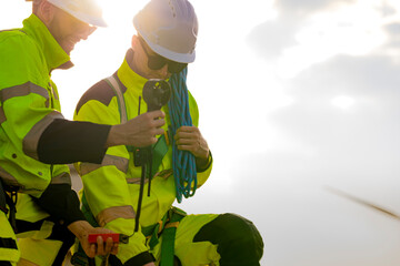 Two engineers wearing high visibility safety jackets and helmets measure wind speed with an...