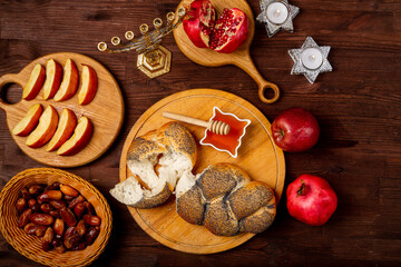 Challah, honey, apple and pomegranate and burning candles on wooden table with menorah Rosh Hashanah
